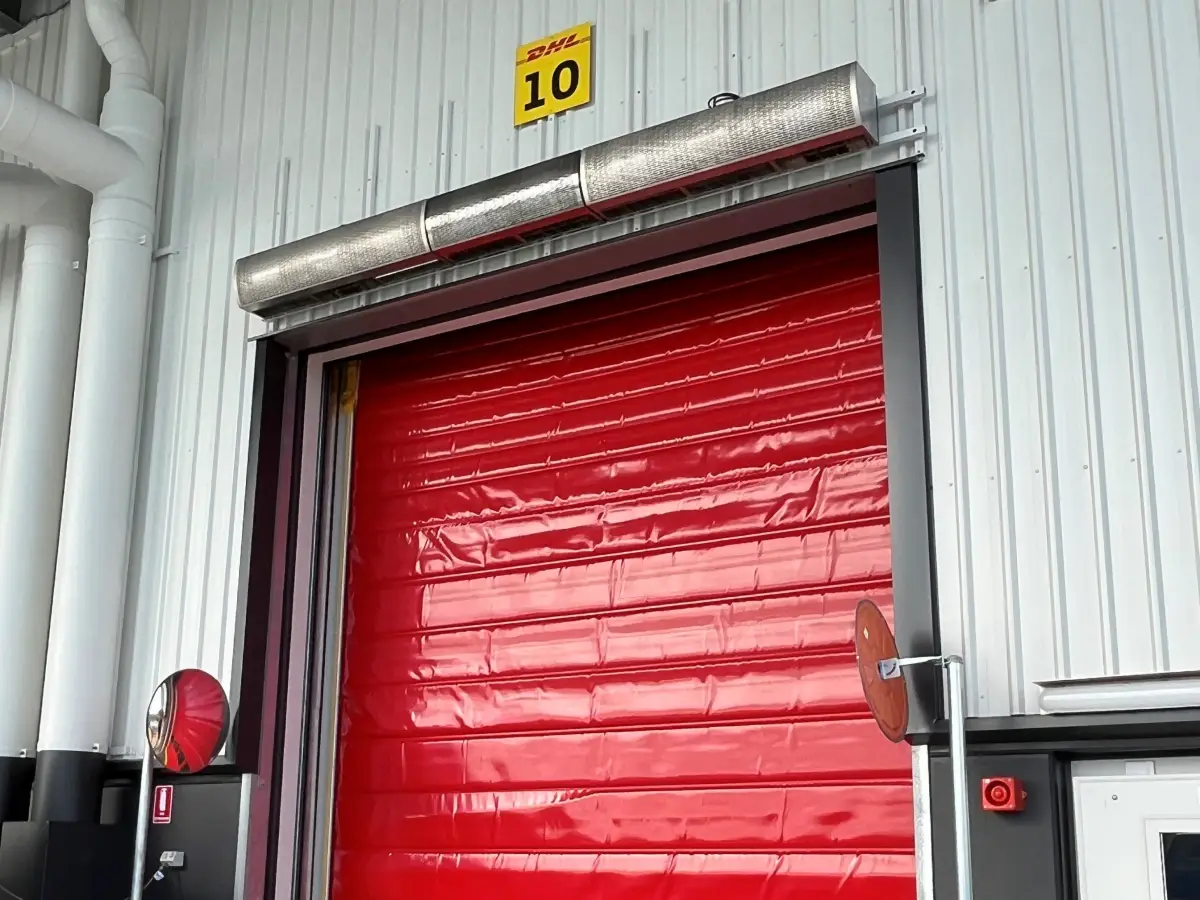 A custom high velocity air barrier industrial air curtain above a rapid-roll high-speed door on the exterior of a warehouse.