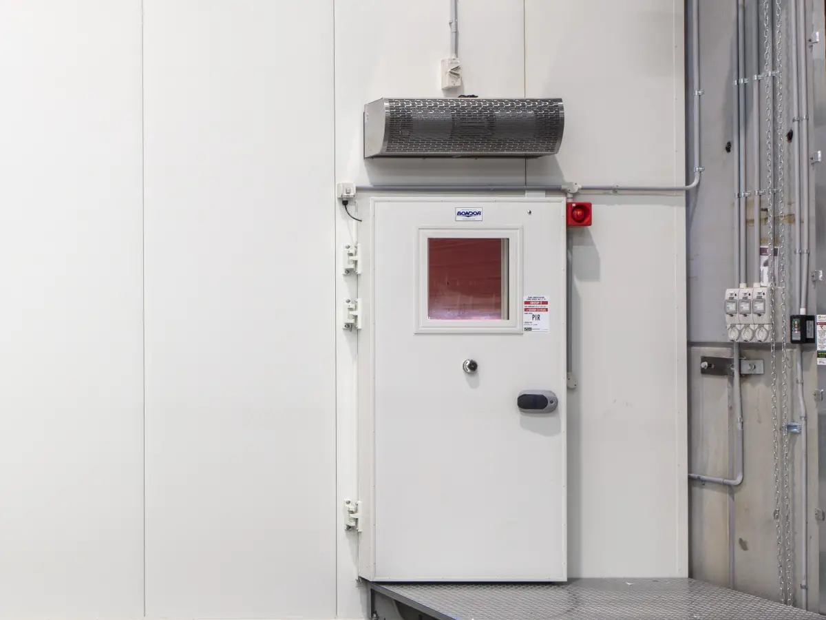 A custom industrial air curtain system above a corrosion-resistant traffic door inside a cold storage refrigeration warehouse.