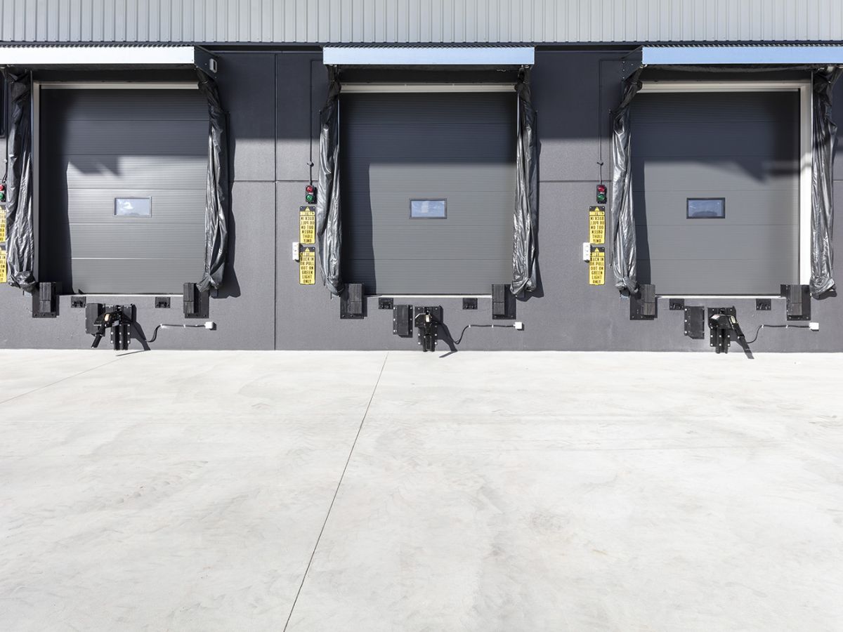 Three large closed sectional doors on a loading dock on the outside of a warehouse.