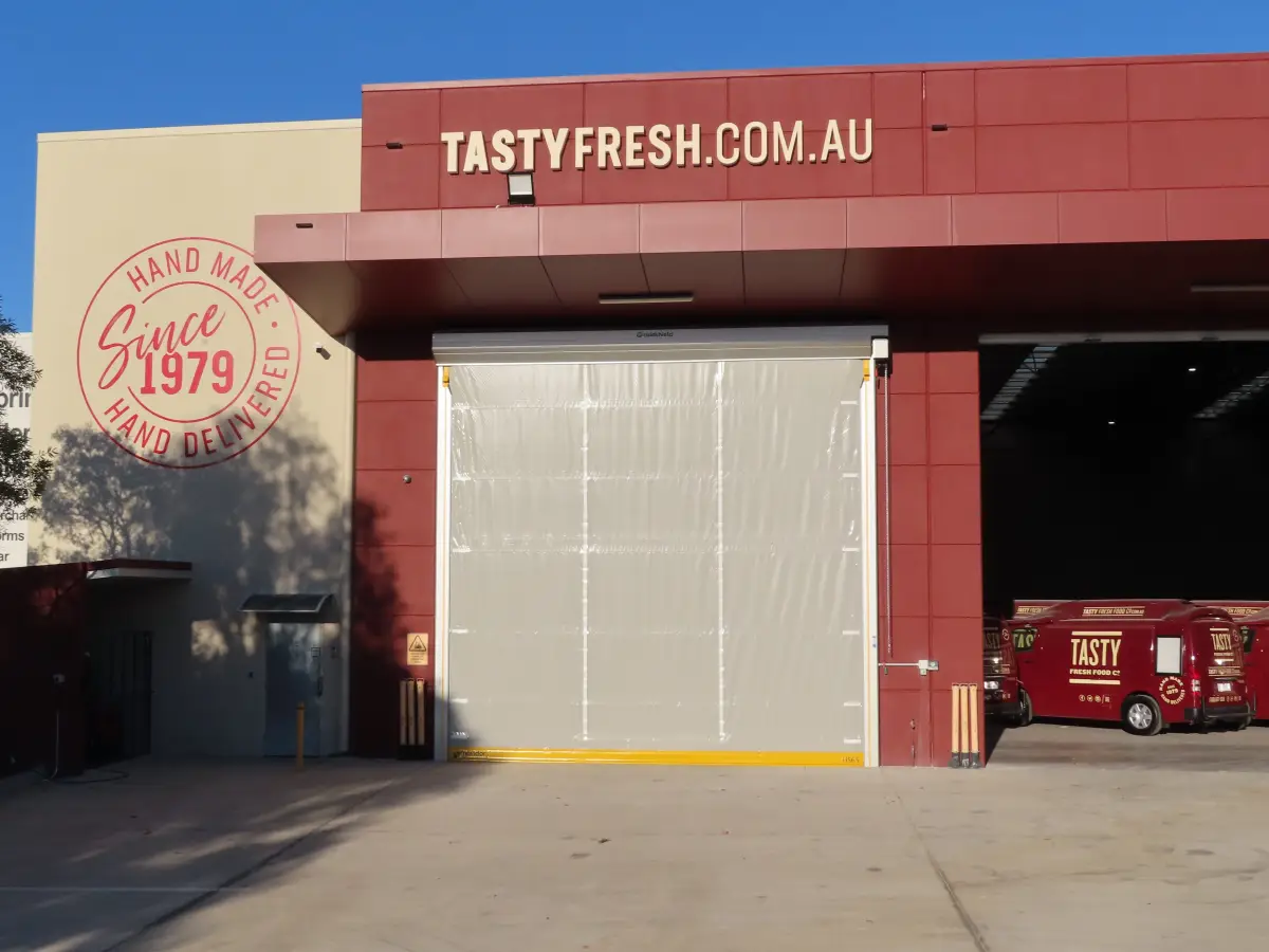 A large Movidor HS65 high speed door on the outside of a food processing factory of Tasty Fresh; the rapid roll door allows efficient building access.