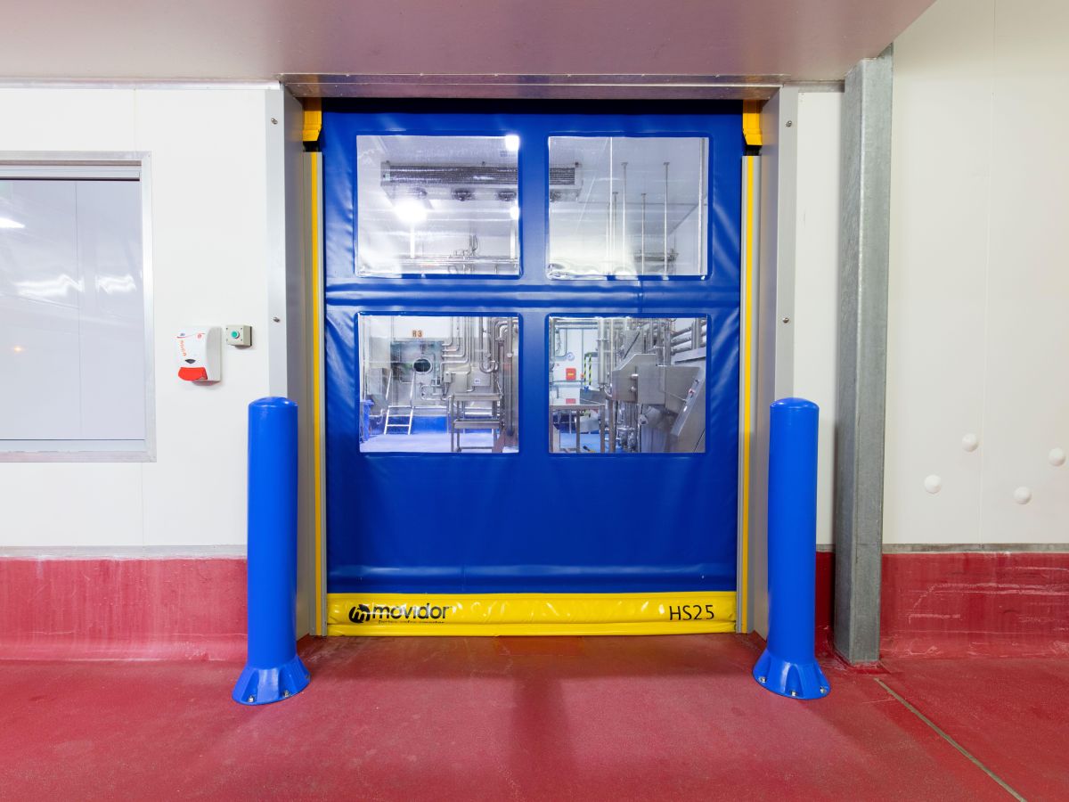 A closed high speed door with two bollards next to it inside a factory.