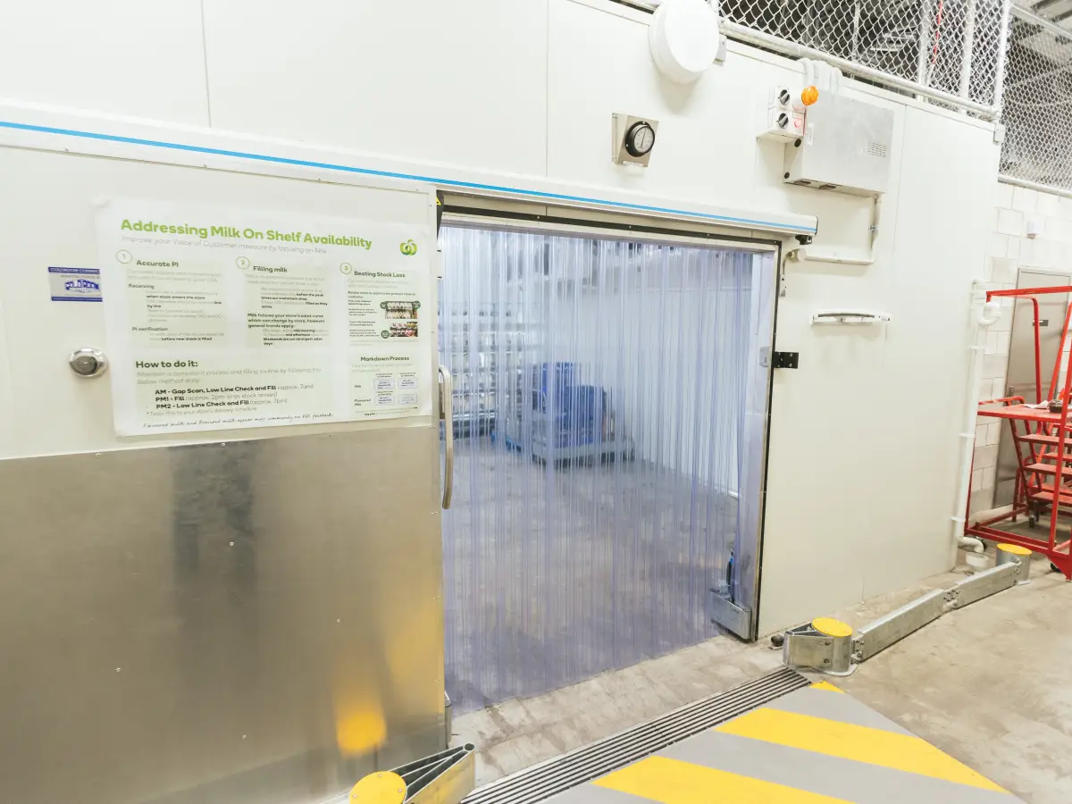 A heavy duty flexible PVC strip curtain installed on an automatic sliding door inside a supermarket backroom.