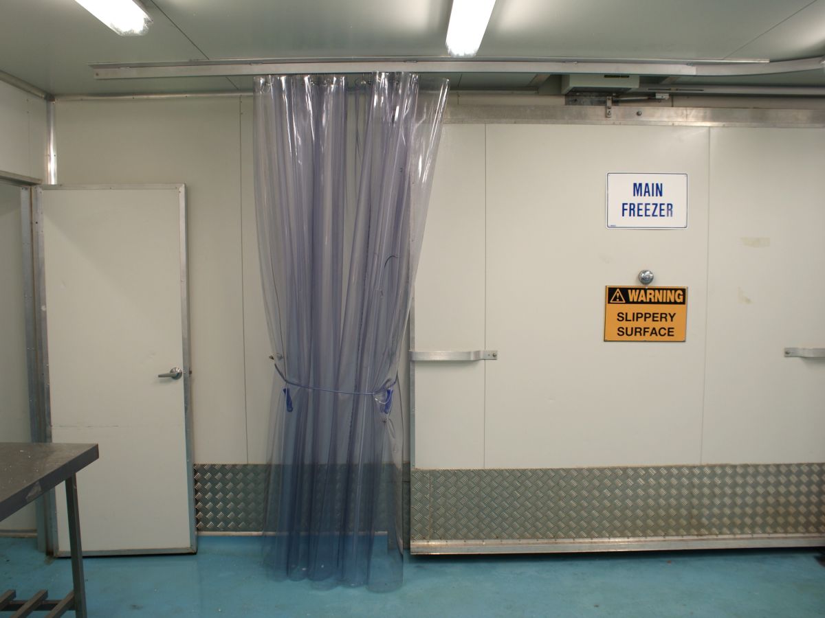 A highly durable, flexible PVC screen curtain pulled to one side, acting as a barrier in a commercial food processing factory.