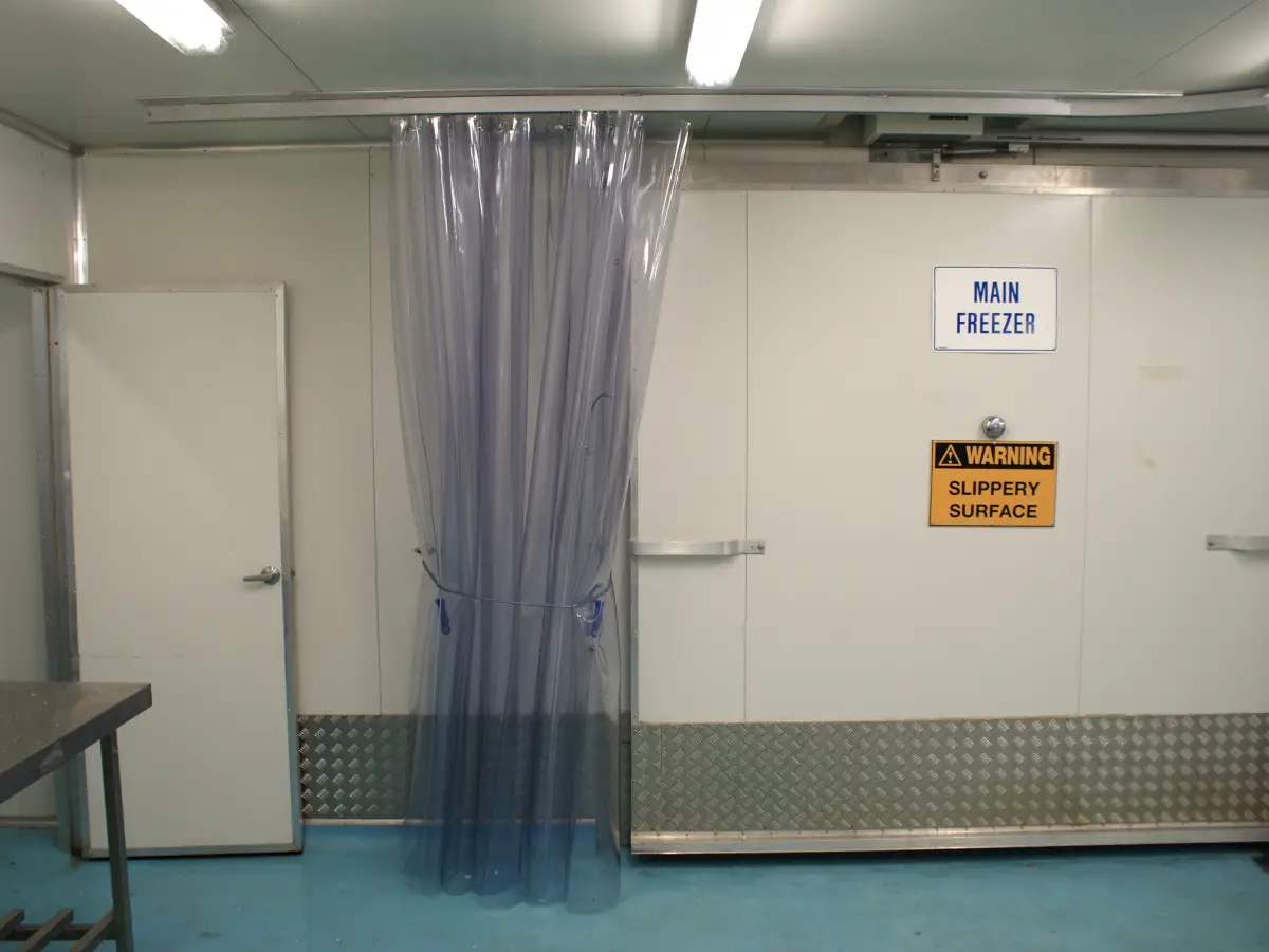 A highly durable, flexible PVC screen curtain pulled to one side, acting as a barrier in a commercial food processing factory.