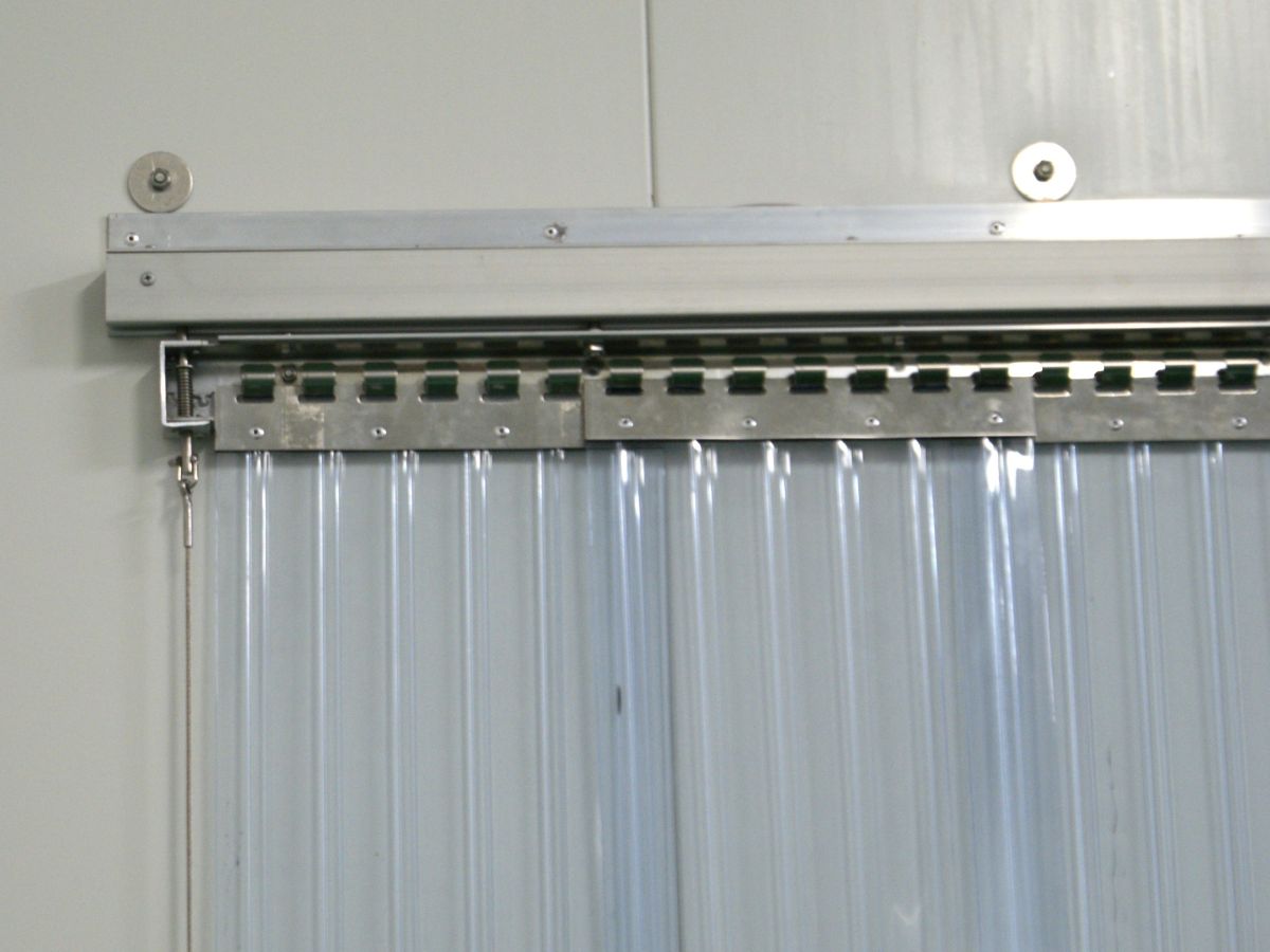 A sliding PVC strip curtain mounting system; clear plastic strips on hooks attached to a sliding cool room traffic door.