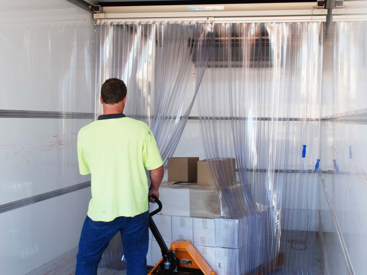 A man removing boxes on a pallet from inside a refrigerated truck through movable PVC strips.