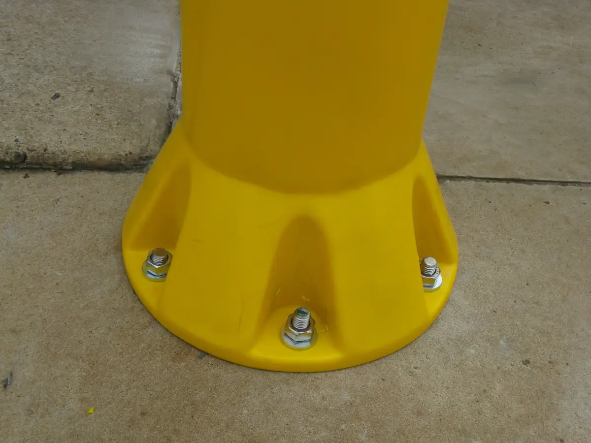 The base of a yellow heavy duty bollard attached to cement; the multiple bollard fixing points shown.