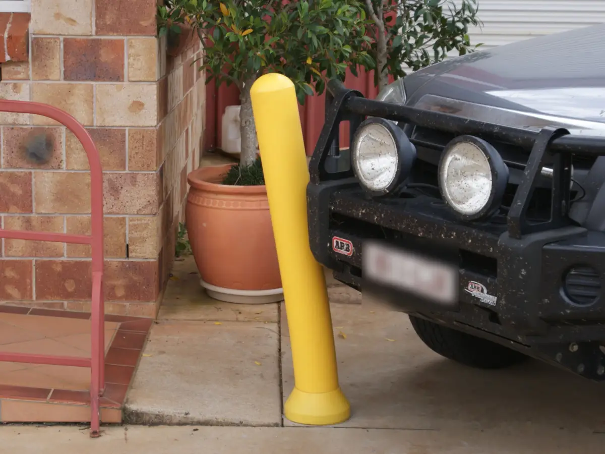 A car hitting a yellow polyethylene bollard; the heavy duty bollard is bending and absorbing the shock.