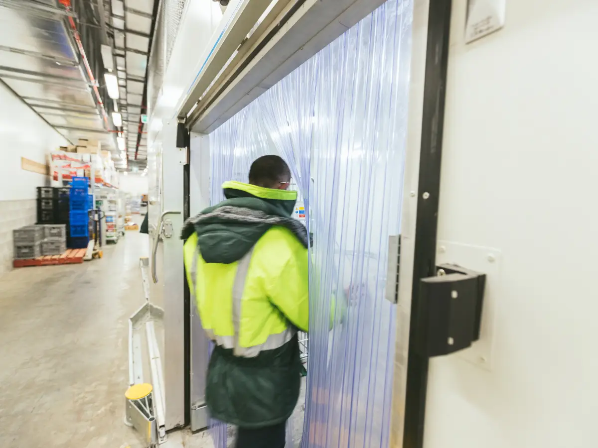 Walking through clear plastic curtains; a PVC door strip to a refrigerated cool room in a retail supermarket.