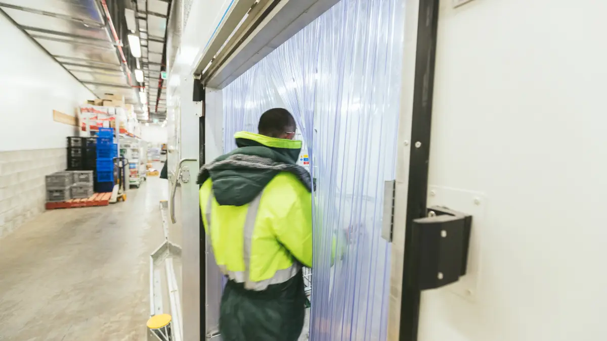 Walking through clear plastic curtains; a PVC door strip to a refrigerated cool room in a retail supermarket.