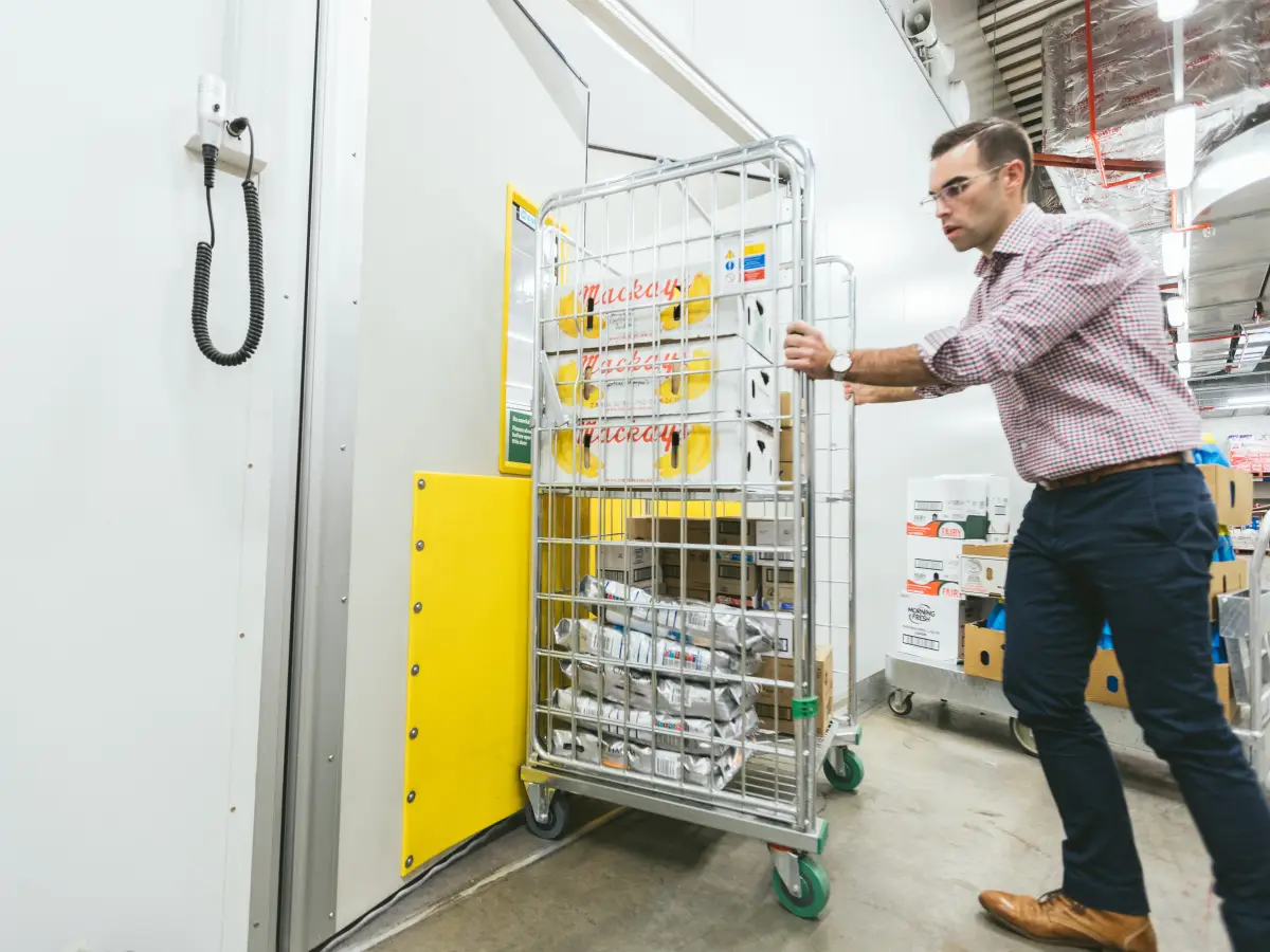A staff member pushing a trolley through a traffic door in a supermarket.