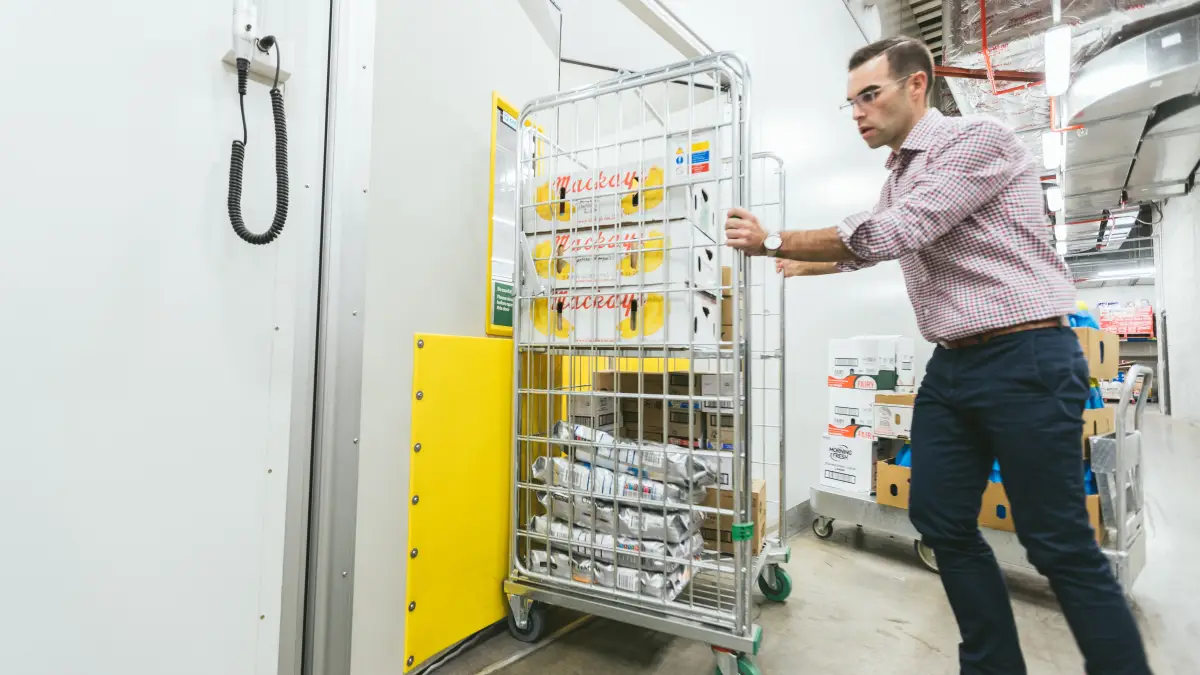 A staff member pushing a trolley through a traffic door in a supermarket.