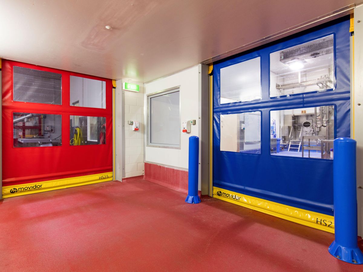 Two closed rapid roll doors with blue bollards in front of one inside an industrial facility.