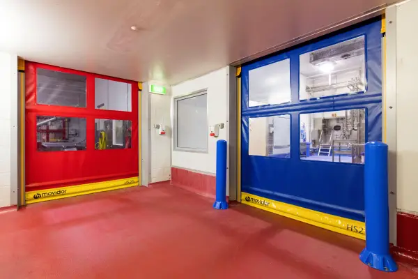 Two closed rapid roll doors with blue bollards in front of one inside an industrial facility.