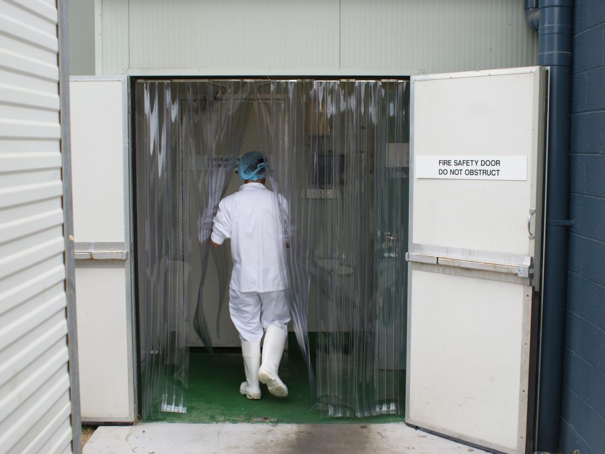 A staff member walking through a PVC strip curtain into a cold room in a food processing factory.