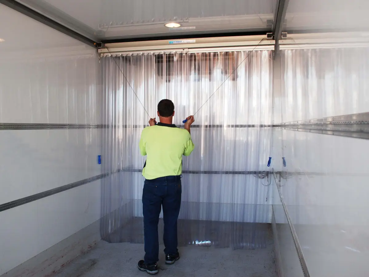 A man adjusting the Compass system of movable clear plastic PVC strip curtains inside a refrigerated truck.
