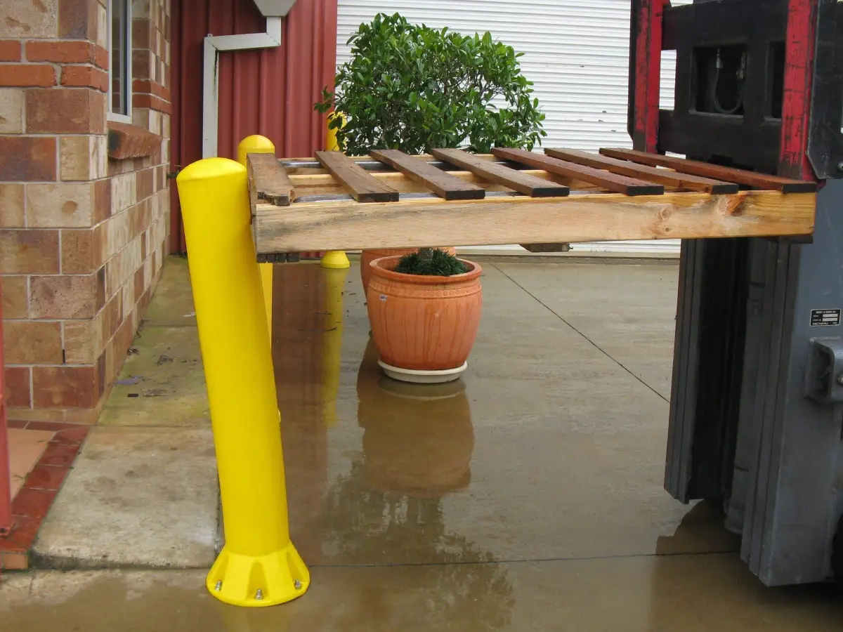 A forklift with a pallet hitting a yellow polyethylene bollard; the heavy duty bollard is bending and absorbing the shock.