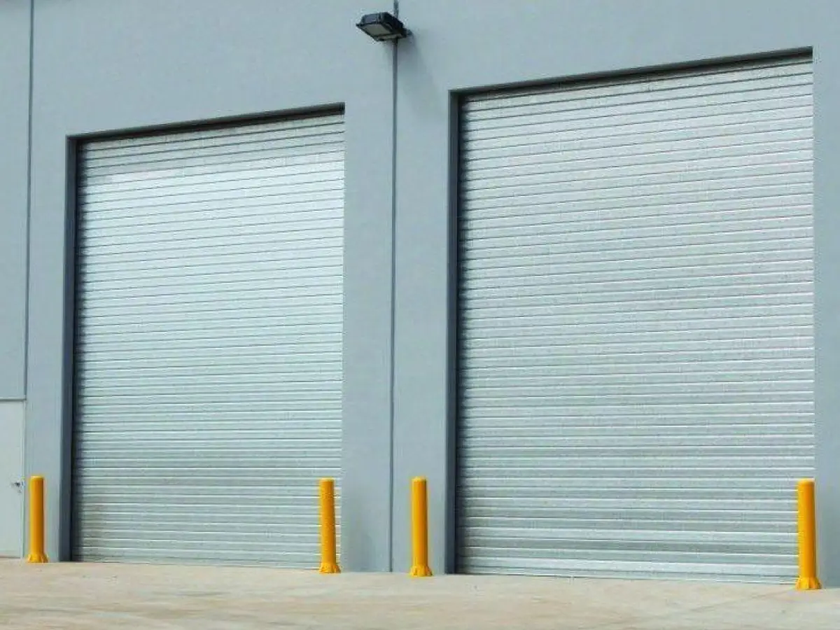 Highly visible bollards set next to industrial roller shutter factory doors; 4 yellow polyethylene bollards for door and wall protection.