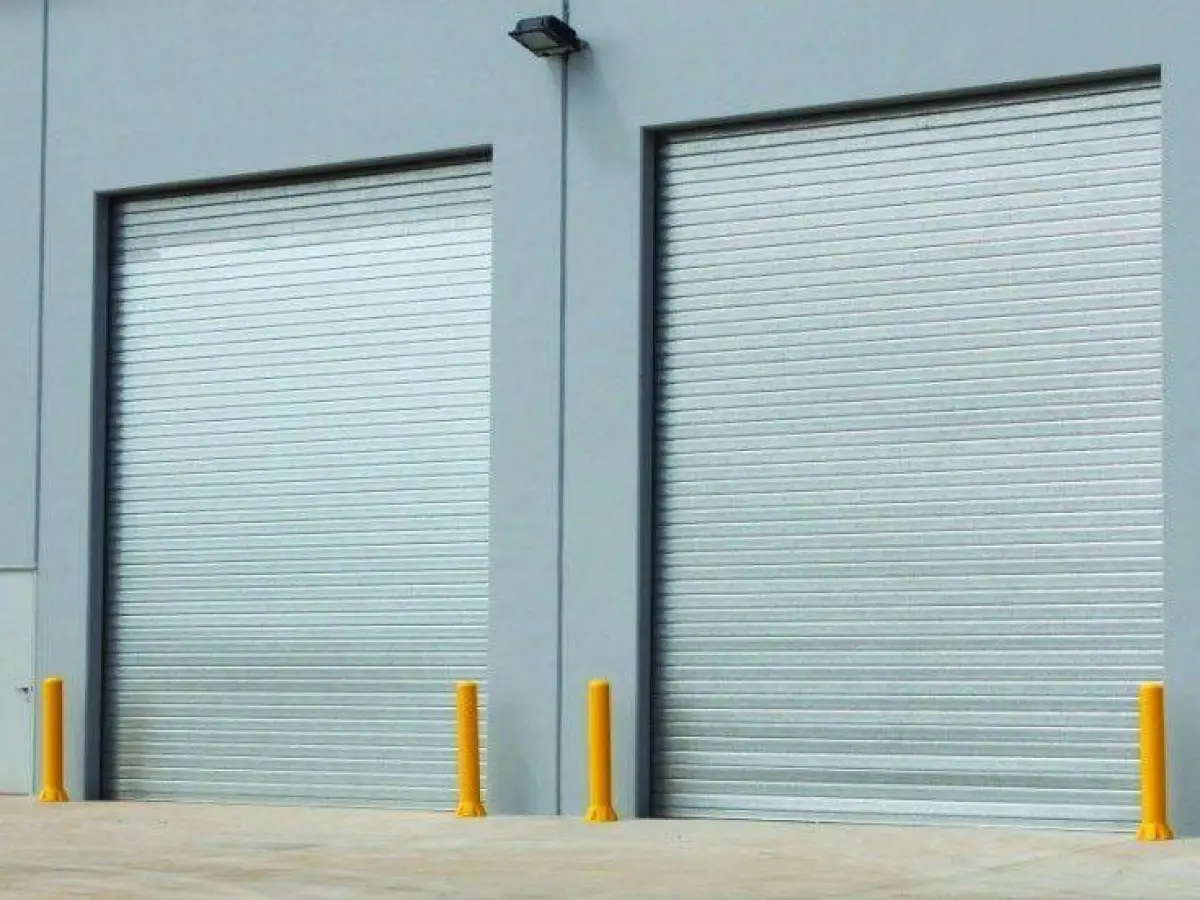 Highly visible bollards set next to industrial roller shutter factory doors; 4 yellow polyethylene bollards for door and wall protection.