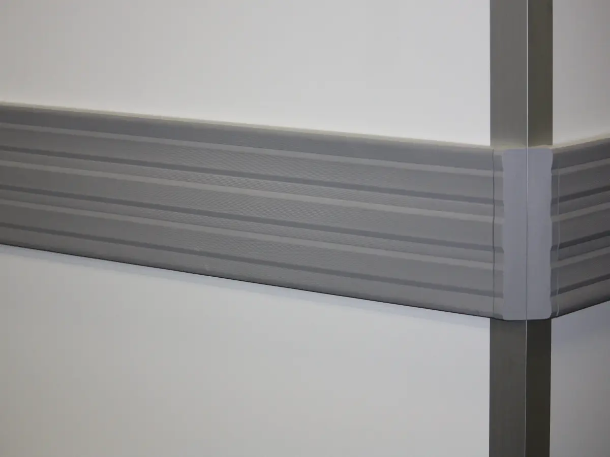 Grey plastic PVC bumprails with grooved finish protecting a wall inside a building.