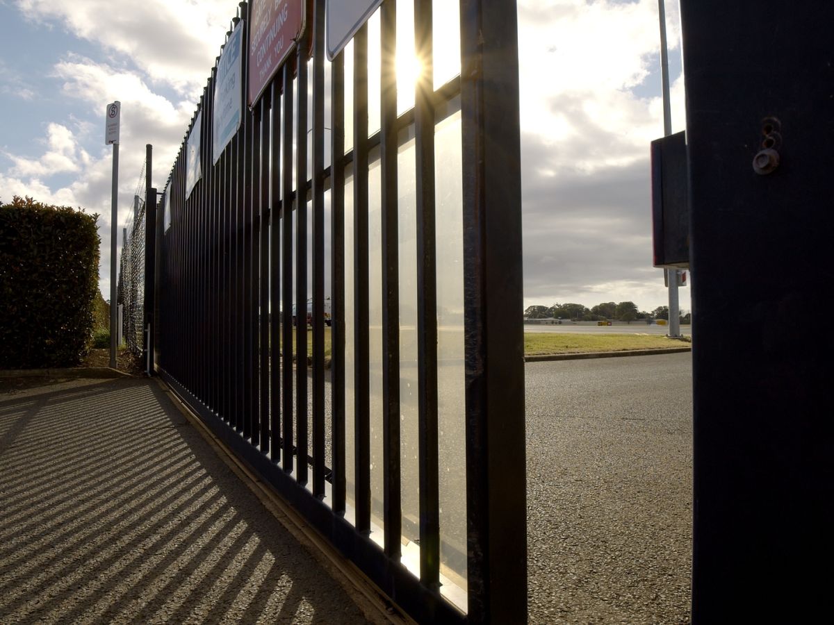A black metal automatic commercial gate starting to open; commercial electric gate for industrial building access.