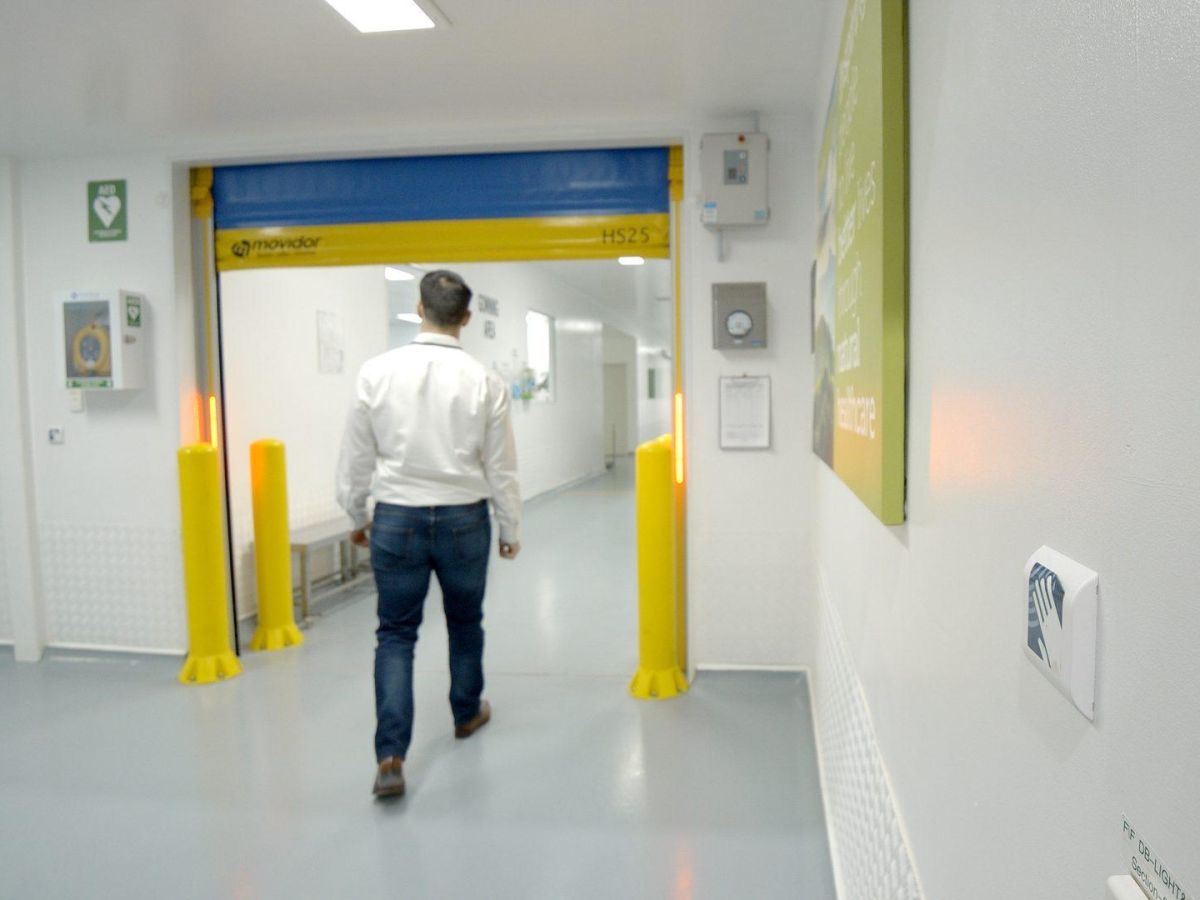 A man walking through an open high speed door in a medical facility with a no touch button in view.