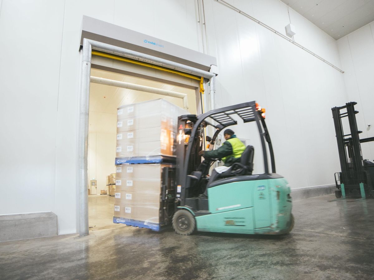 A forklift entering a cold storage room through an open high speed door with two pallets of goods.
