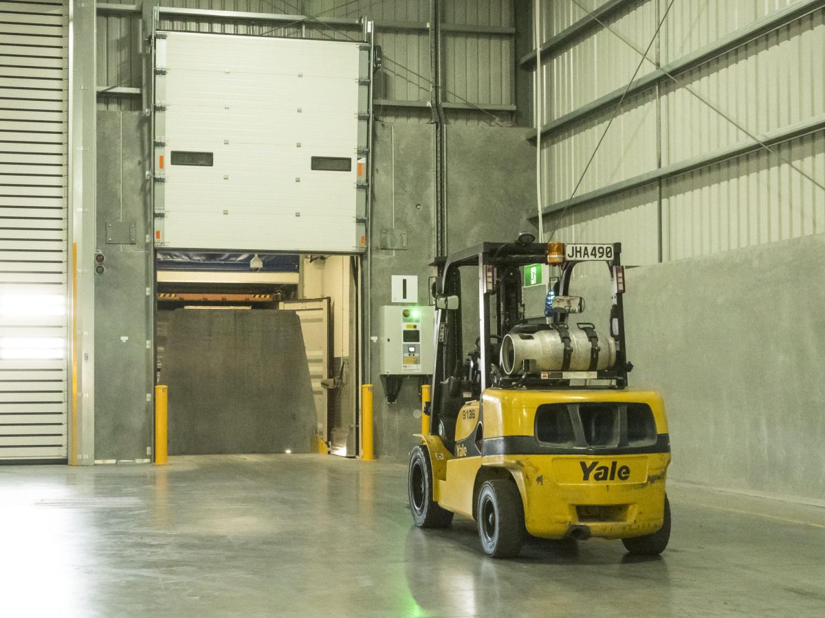 An open section door inside a factory with a forklift about to drive through.