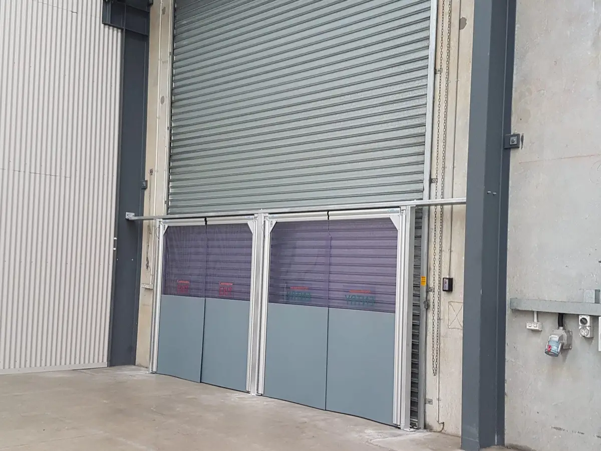 Two PVC swing doors in front of a roller door in an industrial facility.