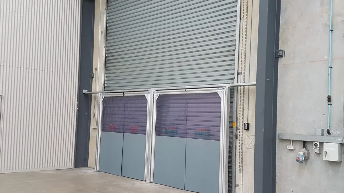 Two PVC swing doors in front of a roller door in an industrial facility.