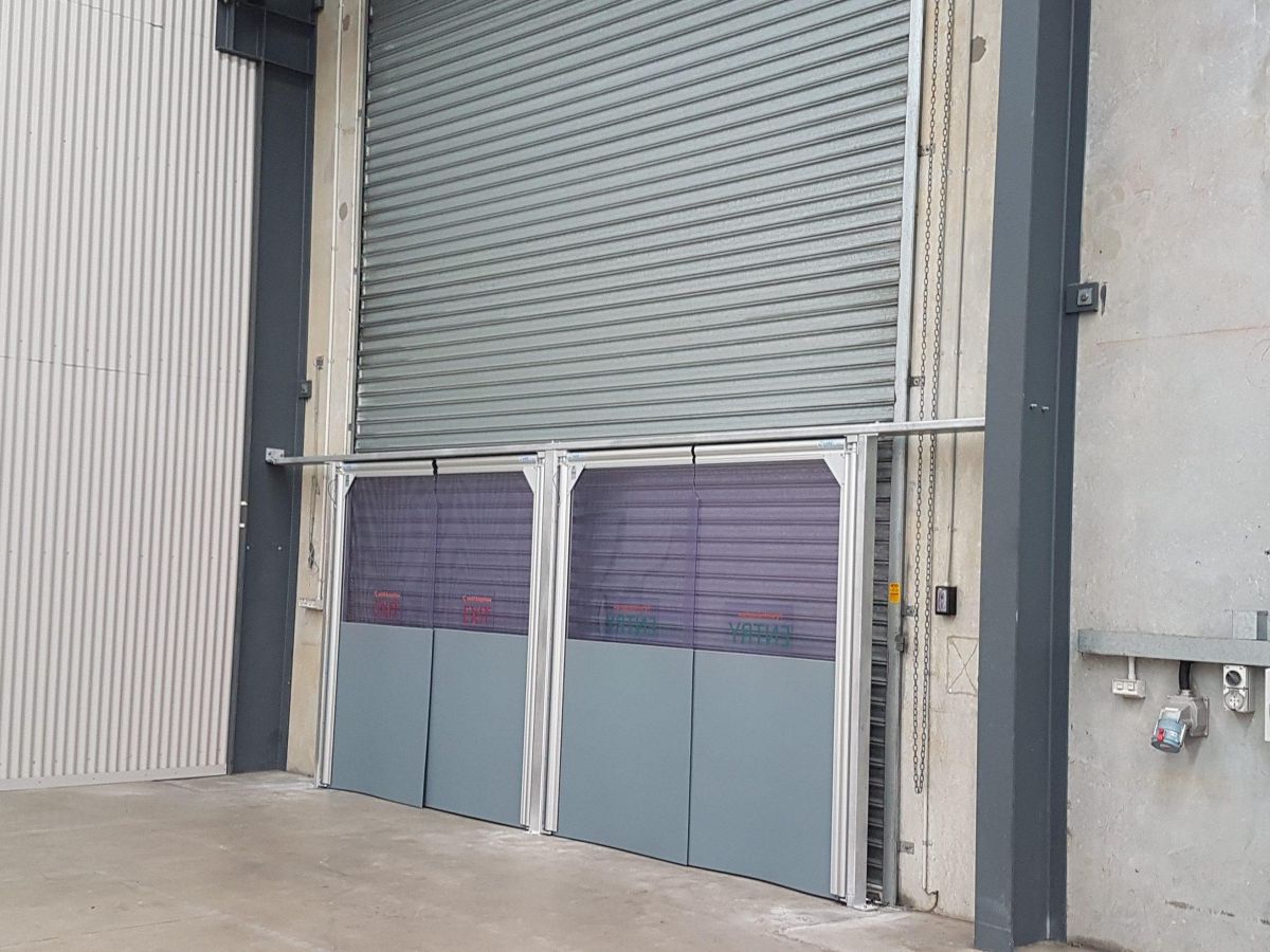 Two PVC swing doors in front of a roller door in an industrial facility.